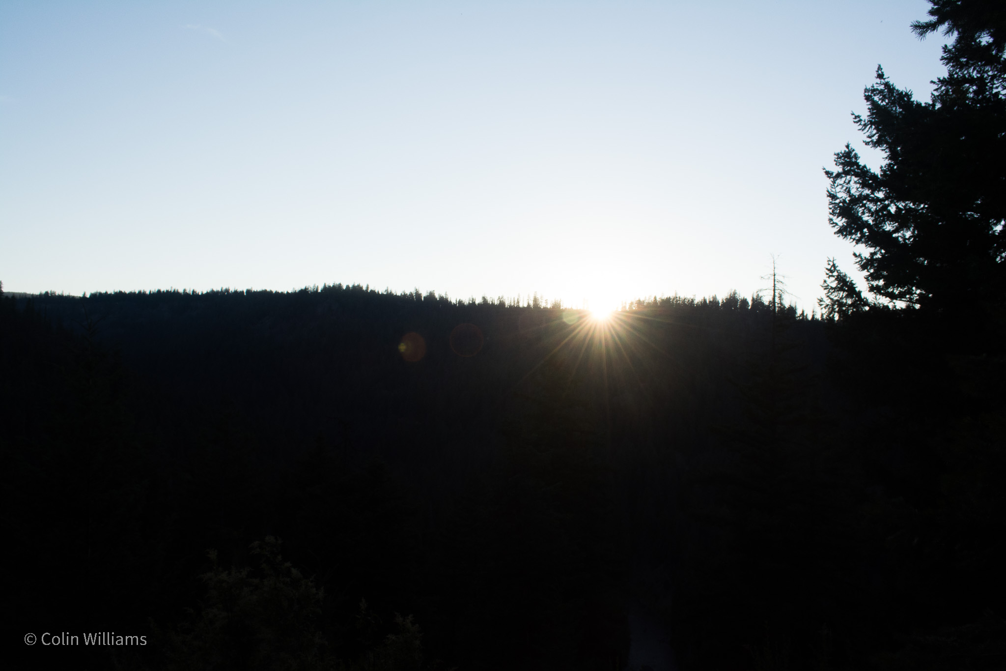 Bright sunrise over a shadowed, forested hill.