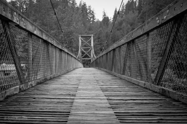 Low view of a wood suspension bridge in black and white.